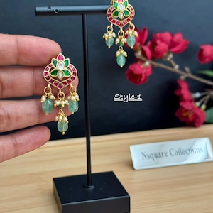 May include: Gold-tone drop earrings featuring a floral-shaped top with green and red enamel accents, a central clear stone, and dangling light green oval beads accented with small white pearls. The text Style-1 is visible in the image.