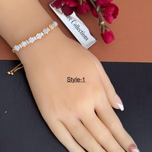 May include: A gold-toned bracelet with a series of clear, sparkling stones in various shapes, including round and marquise cuts. The bracelet is displayed on a mannequin hand. The text "Style-1" is visible.