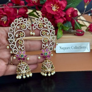 Peut inclure: Une paire de boucles d'oreilles dorées avec des motifs floraux et de feuilles complexes. Les boucles d'oreilles présentent des pierres précieuses claires et colorées, dont des pierres vertes et roses, et de petites perles pendantes. Les boucles d'oreilles ont une base en forme de cloche.
