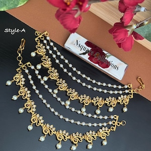 May include: A gold-toned multi-layered ear chain featuring intricate metalwork, small white beads, and clear stones. The piece includes a hook clasp and is labeled Style-A with a silver rectangular tag reading Nsquare Collections.