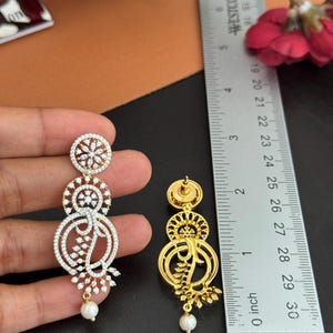 Pu&ograve; includere: Eleganti orecchini dorati e con strass, con un design a tre livelli. Gli orecchini presentano un motivo floreale e una perla pendente. Il righello misura fino a 7.6 cm.