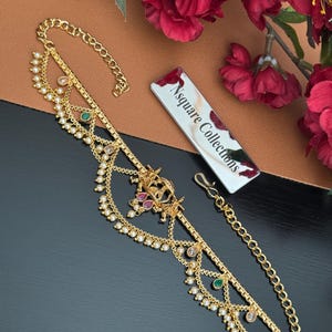 May include: Gold-toned headpiece with pearl and gemstone accents. The design features multiple strands, a central decorative element, and a chain for securing. The headpiece is adorned with small pearls and colorful gemstones. The tag reads "Nsquare Collections".