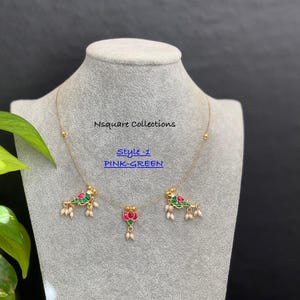 May include: A gold chain necklace with three pendants. The pendants are decorated with green and pink enamel and feature a bird and a lotus flower design. The necklace is labelled "Style 1 PINK-GREEN".
