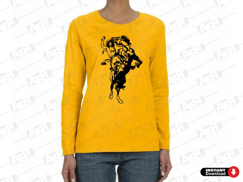 May include: A mustard yellow long-sleeve shirt featuring a black graphic print of a cowboy riding a bucking horse. The shirt has a crew neckline and is paired with blue denim jeans. The design depicts a rider in a hat on a rearing horse.