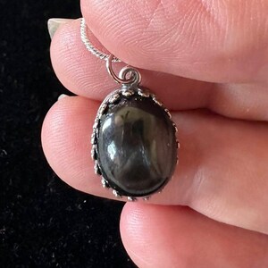 May include: A silver chain necklace with a black oval gemstone pendant. The pendant has a silver filigree border.