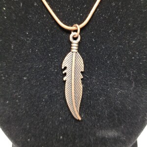 May include: A copper chain necklace with a copper feather pendant.