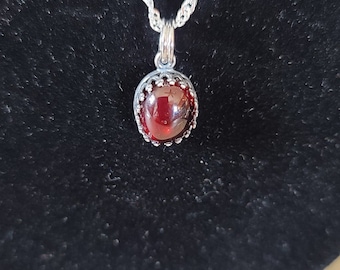 May include: A silver chain necklace with a red gemstone pendant. The pendant is set in a silver bezel with a decorative border.