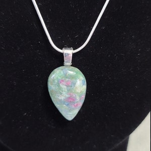 May include: A silver chain necklace with a teardrop-shaped pendant made of green, pink, and white gemstone.