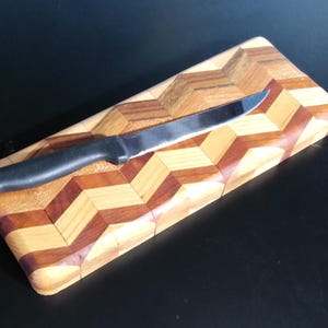 Könnte beinhalten: Ein Messerhalter aus Holz mit einem geometrischen Zickzackmuster in Hell- und Dunkelbraun. Ein Edelstahlmesser mit schwarzem Griff liegt auf der Holzoberfläche.