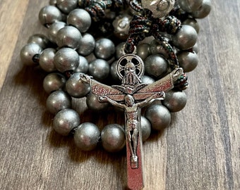 May include: A rosary with large, gray beads and a silver crucifix. The beads are strung on a cord with a decorative knot. The crucifix features a detailed depiction of Jesus Christ.