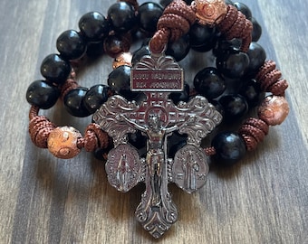 May include: A black wooden rosary with brown cord and a silver crucifix featuring the words "Jesus Nazareno" and "Rex Judæorum".