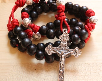 May include: A black wooden rosary with red cord and silver beads. The rosary has a silver crucifix with a figure of Jesus Christ.
