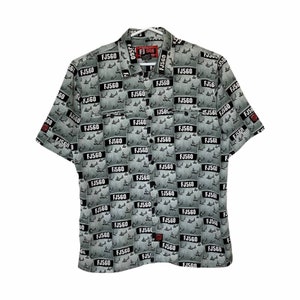 Peut inclure: Une chemise à manches courtes à boutons avec un motif gris et noir d'avions et le texte "FJ560".