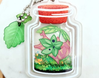 May include: A clear glass jar charm with a silver chain. The jar contains a green plant, a pink and white creature, and green glitter. The jar has a red lid.