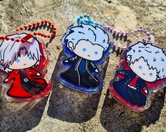 May include: Three acrylic keychains featuring chibi-style characters with white hair and blue eyes. The left keychain has a red ball chain, the center has a blue ball chain, and the right has a purple ball chain, each depicting a unique outfit.