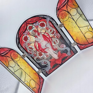 May include: A triptych with a stained-glass design. The central panel shows a figure with long red hair, roses, and serpents. The side panels have abstract patterns in red, orange, and yellow. Silver metal hinges connect the panels.