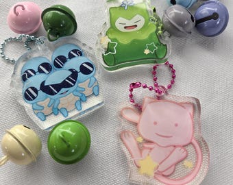 May include: Three clear acrylic charms featuring cartoon characters, including a group of blue turtles with sunglasses, a green creature with a flower, and a pink feline-like figure, accompanied by several small colorful metal jingle bells.