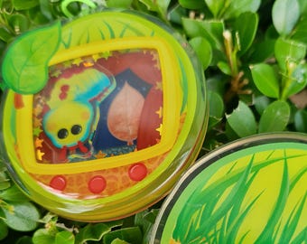 May include: A green and yellow plastic toy with a screen showing a cartoon butterfly and a leaf. The toy has a red button on the bottom.