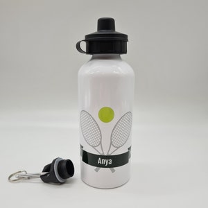 May include: White aluminum water bottle with a black lid and a black carrying loop. The bottle has a tennis racket and ball design with the name "Anya" printed on a black banner.