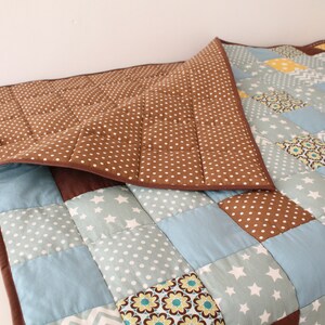 May include: A brown and blue patchwork quilt with a brown polka dot backing. The quilt is made of various fabrics with different patterns, including stars, flowers, and geometric shapes.
