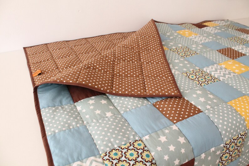 May include: A brown and blue patchwork quilt with a brown polka dot backing. The quilt is made of various fabrics with different patterns, including stars, flowers, and geometric shapes.