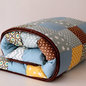 May include: A blue and brown patchwork quilt with a variety of patterns, including stars, polka dots, and flowers.