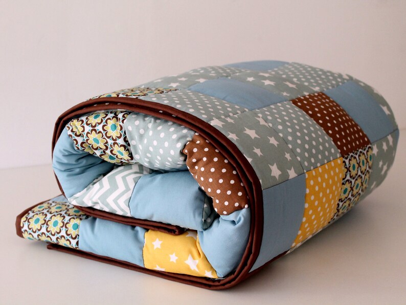 May include: A blue and brown patchwork quilt with a variety of patterns, including stars, polka dots, and flowers.