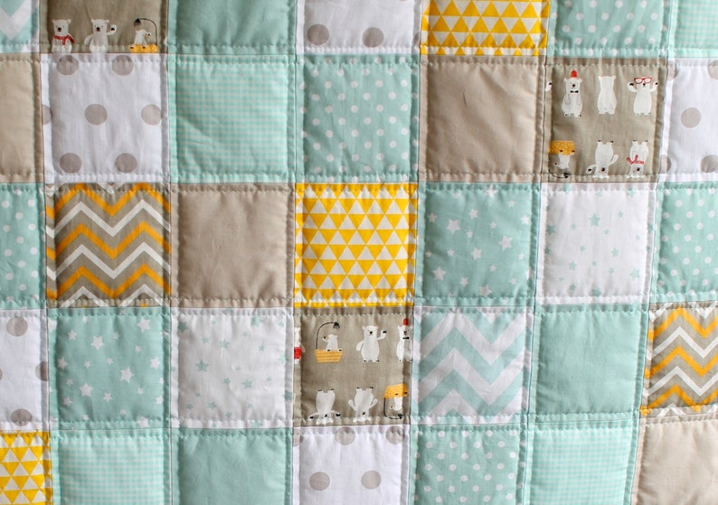 May include: A patchwork quilt with a variety of patterns in shades of gray, white, yellow, and light blue. The patterns include polka dots, stars, chevron, and geometric shapes.