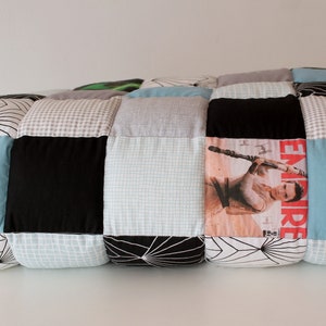 May include: A patchwork quilt made of various fabrics, including black, white, gray, and blue. The quilt is rolled up and features a magazine cover with a woman holding a lightsaber.