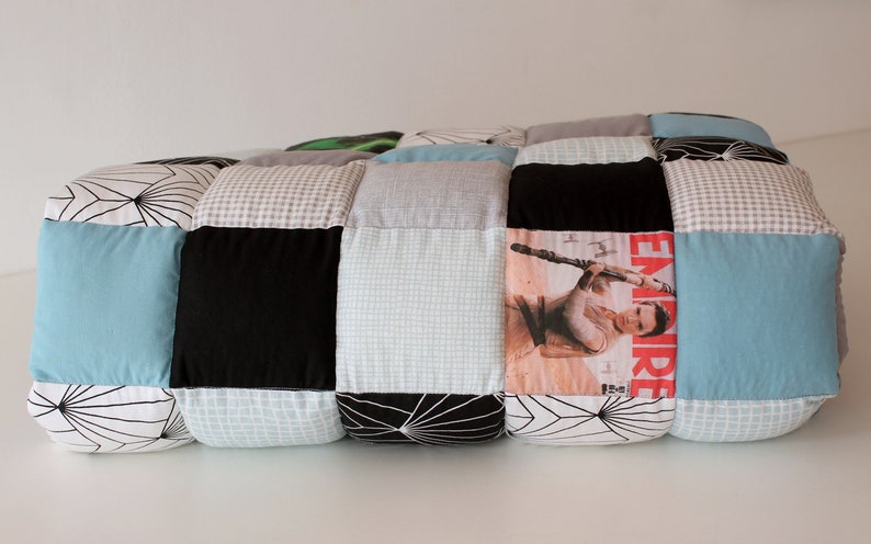 May include: A patchwork quilt made of various fabrics, including black, white, gray, and blue. The quilt is rolled up and features a magazine cover with a woman holding a lightsaber.