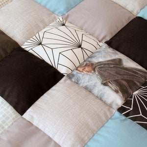 May include: A patchwork quilt with a variety of fabrics, including black, white, gray, and blue. One square features a black and white geometric pattern, another square features a photo of a man in a brown robe, and another square features a blue and white checkered pattern.