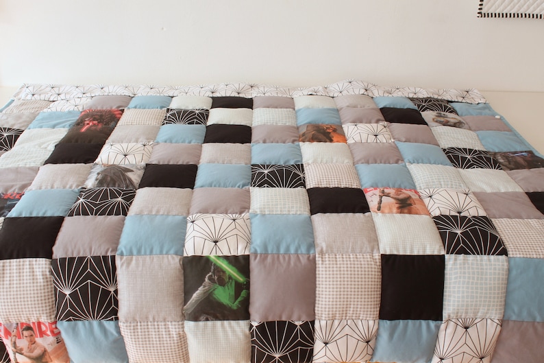 May include: A patchwork quilt with a variety of patterns and colors, including black, white, gray, blue, and brown. The quilt is made up of squares, and some of the squares have images printed on them.