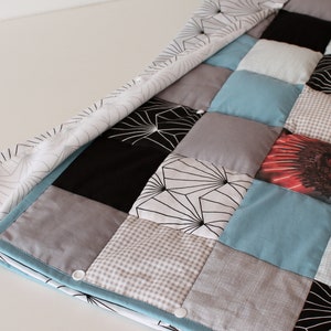 May include: A patchwork quilt with a variety of patterns and colors, including black, white, gray, blue, and red. The quilt is made of different fabrics, including cotton and flannel. The quilt is folded in half and has a white background.