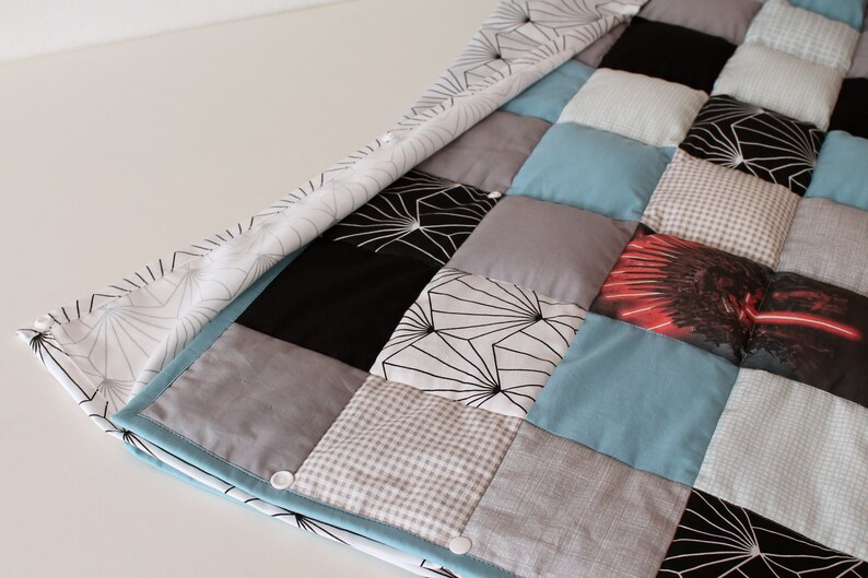 May include: A patchwork quilt with a variety of patterns and colors, including black, white, gray, blue, and red. The quilt is made of different fabrics, including cotton and flannel. The quilt is folded in half and has a white background.
