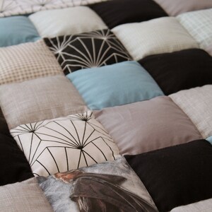 May include: A patchwork quilt with various patterns and colors, including black, white, gray, and blue. The quilt is made of squares and rectangles, and some of the squares have geometric designs.