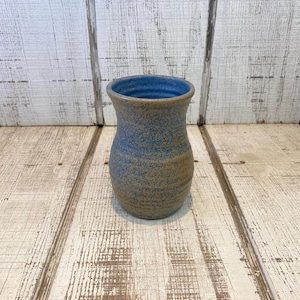 May include: A ceramic vase with a flared rim and a rounded body. The exterior features a speckled tan and blue finish, while the interior is glazed in a solid, vibrant blue. The vessel has a smooth, curved silhouette and a wide, open top.