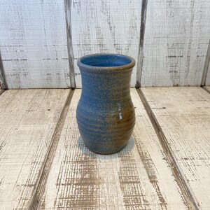 May include: A ceramic vase with a flared rim and a rounded body. The exterior features a speckled blue glaze on the upper portion that transitions into a warm brown tone at the base. The interior of the vase is finished in a solid blue glaze.
