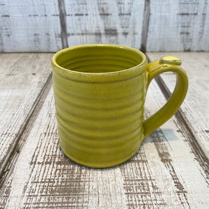 May include: A yellow ceramic mug with a rounded handle. The mug has a textured, ribbed design.