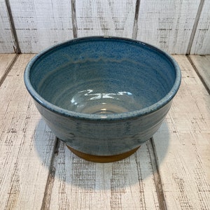 May include: A large, blue ceramic bowl with a speckled glaze. The bowl has a wide rim and a rounded base. It is sitting on a wooden surface.