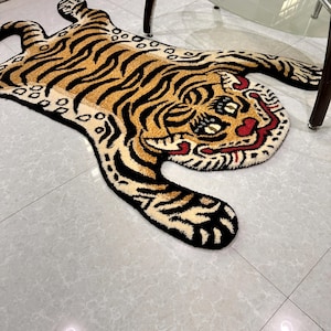 May include: A tiger rug with a black and orange striped pattern. The tiger's face is detailed with black eyes, a red mouth, and a white nose.