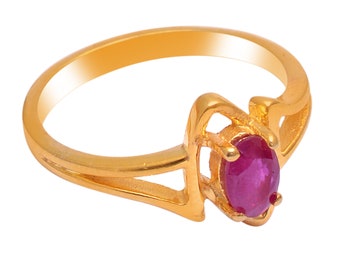 Può includere: Un anello d'oro con una gemma ovale rosso scuro. L'anello ha un design a gambo diviso con un'incastonatura decorativa attorno alla gemma. L'anello è posto su uno sfondo bianco.
