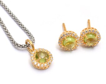 May include: A gold necklace with a green gemstone pendant surrounded by small clear stones. Matching earrings with green gemstones and clear stones.