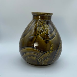 May include: A brown ceramic vase with a rounded body and a wide mouth. The vase is decorated with a swirling pattern of raised lines and a fish design.