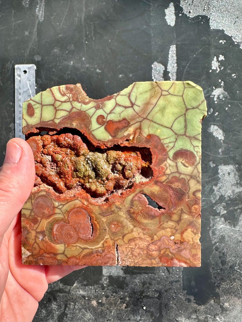 Puede incluir: Una pieza de &aacute;gata pulida verde y roja con un patr&oacute;n &uacute;nico de vetas y remolinos. La &aacute;gata tiene un borde natural, &aacute;spero y una superficie lisa y pulida.