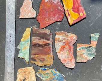 Puede incluir: Surtido de láminas de ágata pulidas en varios colores y patrones, incluyendo rojo, amarillo, verde, azul y marrón. Las láminas están dispuestas sobre una superficie gris.