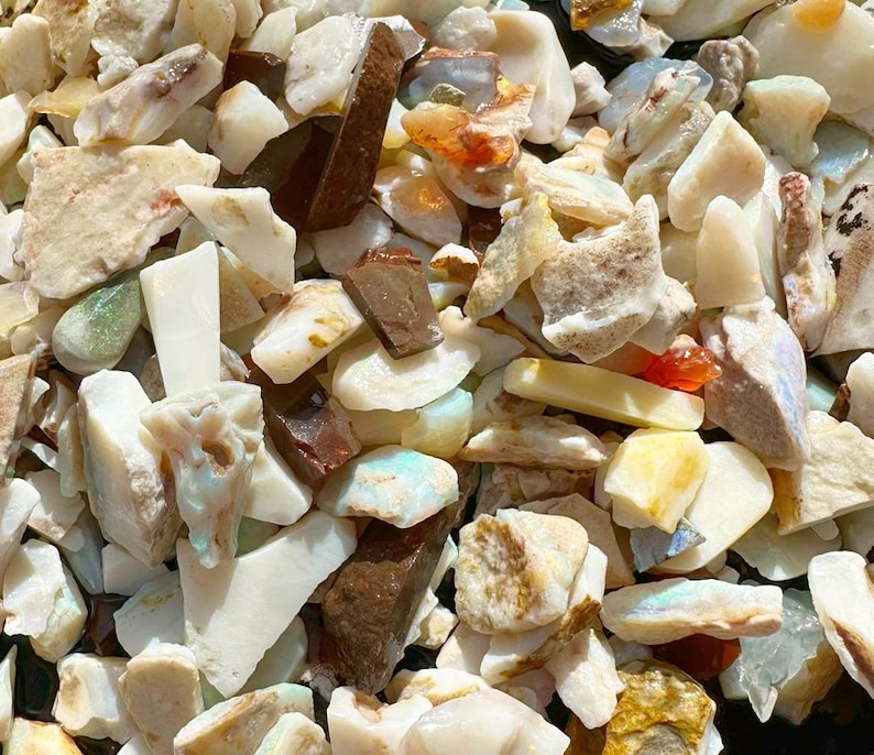 K&ouml;nnte beinhalten: Nahaufnahme eines Haufens roher Opalsteine. Die Steine variieren in der Farbe, darunter Wei&szlig;, Braun, Orange und Hauch von Blau und Gr&uuml;n. Die raue, nat&uuml;rliche Textur der Steine ist sichtbar, wobei einige St&uuml;cke durchscheinend erscheinen.