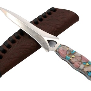 Puede incluir: Una daga de plata con un mango de piedras preciosas rosas y turquesa y una funda de cuero.