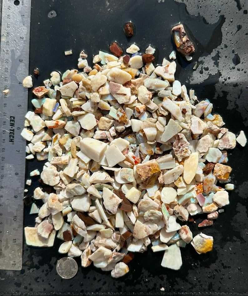 K&ouml;nnte beinhalten: Ein Haufen roher, ungeschliffener Opal-Edelsteine in verschiedenen Formen und Gr&ouml;&szlig;en. Die Steine zeigen eine Reihe von Farben, darunter Wei&szlig;, Braun und Ankl&auml;nge von Blau und Rot. Ein Metalllineal mit Zentimetermessungen ist sichtbar.