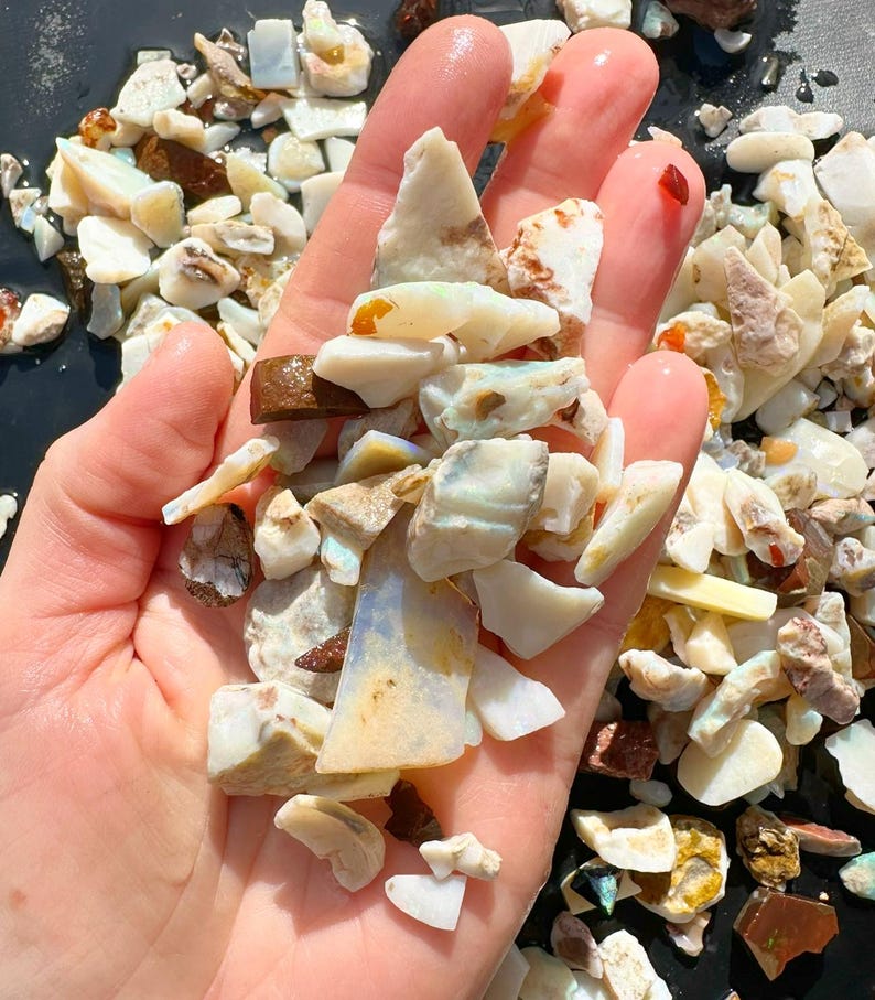 K&ouml;nnte beinhalten: Eine Handvoll roher Opal-Edelsteine in verschiedenen Formen und Gr&ouml;&szlig;en. Die Opale zeigen eine Reihe von Farben, darunter Wei&szlig;, Creme, Braun und Andeutungen von Blau und Orange. Die Edelsteine sind grob geschnitten und scheinen nat&uuml;rlich zu sein, f&uuml;r die Schmuckherstellung.