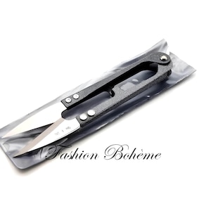 Può includere: Un paio di forbici per stoffa nere e argentate in una custodia di plastica. Le forbici sono chiuse e la custodia è piegata.